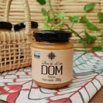 Doce de leite DOM em pote pequeno com 290 gramas, sobre mesa de madeira.