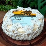Queijo Moldura de Minas embalado em capa de crochê, sobre mesa de madeira.