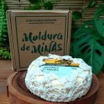 Queijo Moldura de Minas embalado em capa de crochê, sobre mesa de madeira.