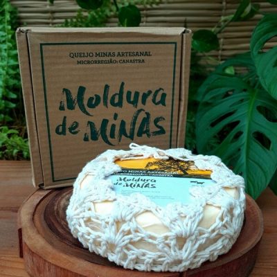 Queijo Moldura de Minas embalado em capa de crochê, sobre mesa de madeira.