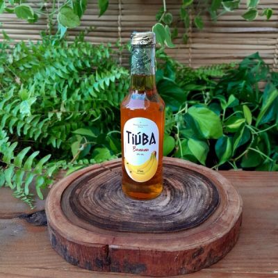 Tiúba Banana em garrafa de 275 ml sobre mesa de madeira.