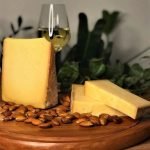 Queijo Comte Serra das Antas sobre tábua de madeira, com taça de espumante.