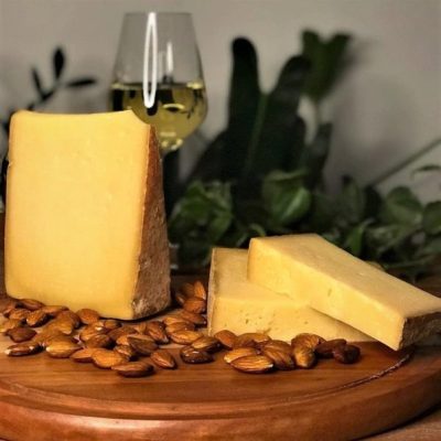 Queijo Comte Serra das Antas sobre tábua de madeira, com taça de espumante.