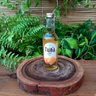 Tiúba mel em garrafa de 275 ml sobre mesa de madeira.
