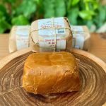 Bala de doce de leite Serra Negra aberta sobre tábua de madeira, com outra bala embalada ao fundo.