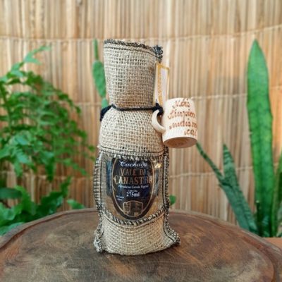 Cachaça Vale da Canastra com copinho de capa de juta, sobre mesa de madeira.