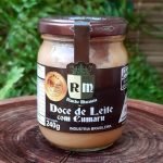Doce de leite com cumaru Rancho Maranata em pote de vidro com 240 gramas sobre mesa de madeira.