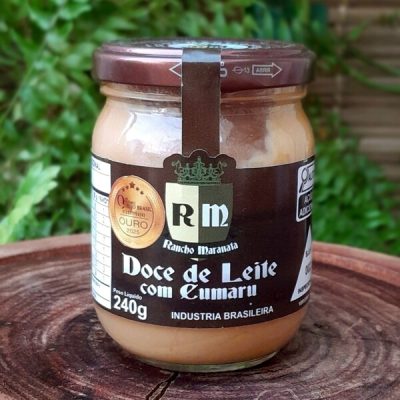 Doce de leite com cumaru Rancho Maranata em pote de vidro com 240 gramas sobre mesa de madeira.