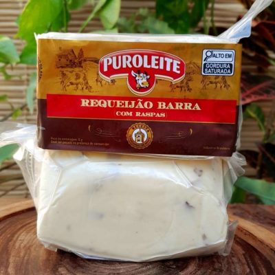 Requeijão em barra com raspas em embalagem de aproximadamente 500 gramas, sobre mesa de madeira.