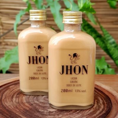 Licor de doce de leite Jhon, produzido com doce de leite DOM, em garrafa de 200 ml sobre mesa de madeira.