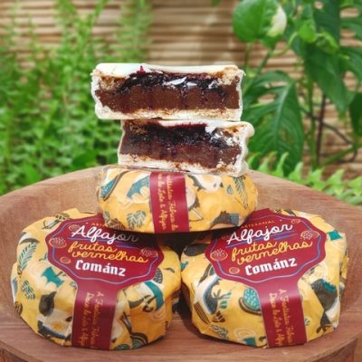 Alfajor Comanz recheado com doce de leite e frutas vermelhas, sobre mesa de madeira.
