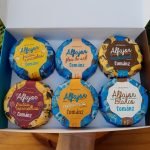 Alfajor Cománz em caixa compondo kit com 6 unidades, sobre mesa de madeira.