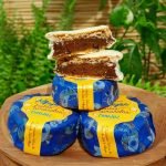 Alfajor Cománz recheado com doce de leite e frutas amarelas, sobre mesa de madeira.