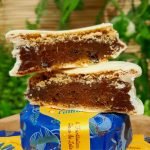 Alfajor Cománz recheado com doce de leite e frutas amarelas, sobre mesa de madeira.
