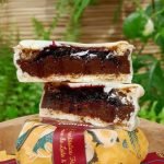 Alfajor Comanz recheado com doce de leite e frutas vermelhas, sobre mesa de madeira.