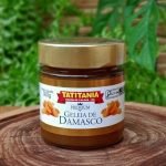 Geleia de damasco Tatitânia em pote de 300 gramas sobre mesa de madeira.