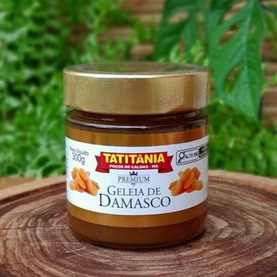Geleia de damasco Tatitânia em pote de 300 gramas sobre mesa de madeira.