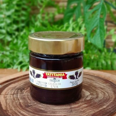 Geleia de uva Tatitânia em pote de 300 gramas sobre mesa de madeira.