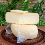 Queijo Vô Bastião meia cura Serra das Antas sobre mesa de madeira.