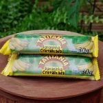 Bananinha cristalizada Tatitânia em embalagem individual de 30 gramas, sobre mesa de madeira.