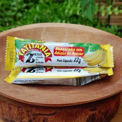 Bananinha sem açúcar Tatitânia, em embalagem individual com 22 gramas, sobre mesa de madeira.