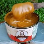 Doce de leite Dona Lázara em lata de 400 gramas, com foto em close do doce em colher de madeira.