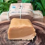 Bala de doce de leite Conquista de 300 gramas, desembrulhada e partida sobre mesa de madeira.