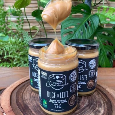 Doce de leite Conquista em pote de vidro com 430 gramas, sobre mesa de madeira.