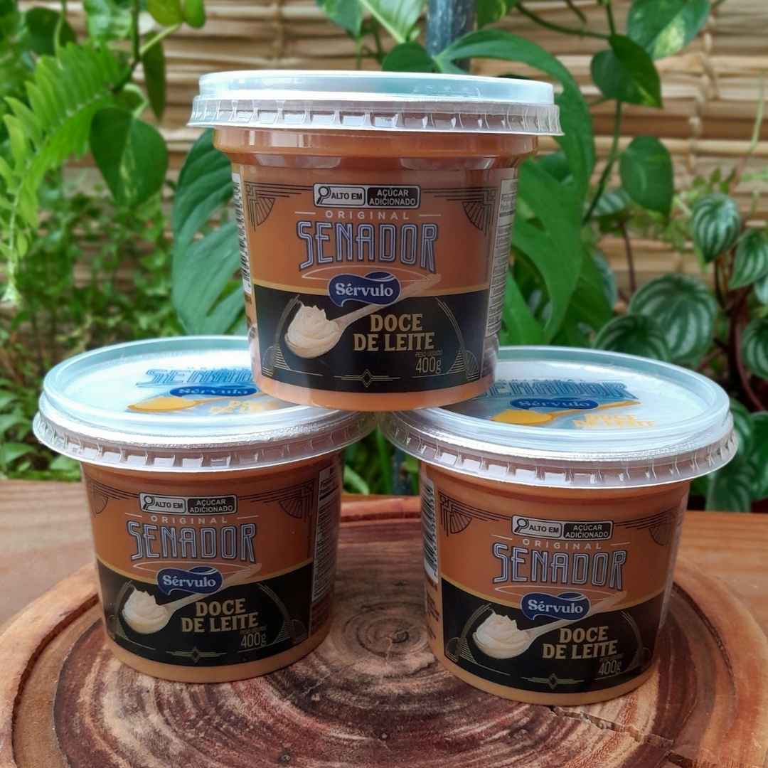 doce-de-leite-senador-400g Doce de leite Senador Sérvulo em pote plástico com 400 gramas, sobre mesa de madeira.