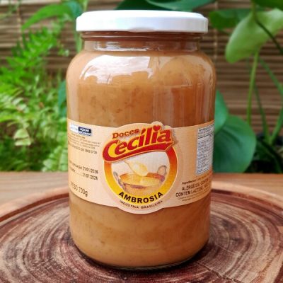 Ambrosia cremosa Doces Cecília em pote de vidro com 700 gramas, sobre mesa de madeira.