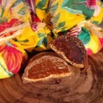 Comanzitos - bombom de chocolate meio amargo recheado com doce de leite Cománz, sobre mesa de madeira.