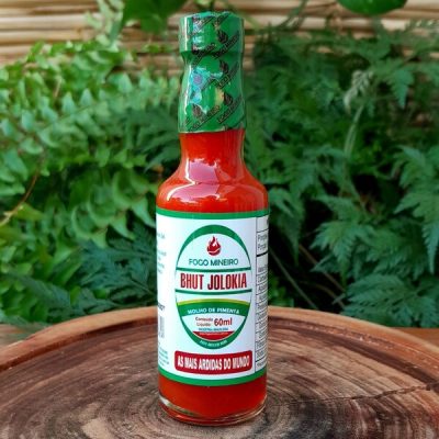 Molho de pimenta Bhut Jolokia em embalagem de vidro com 60 ml sobre mesa de madeira.