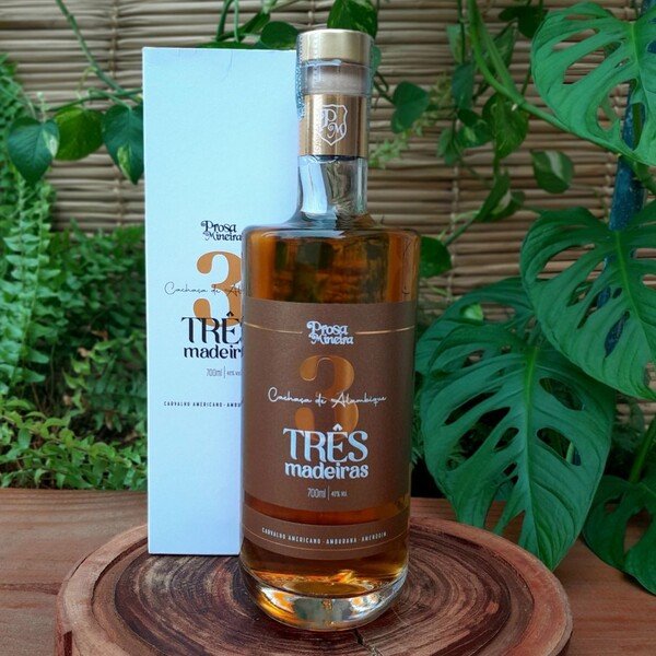 cachaca-tres-madeiras Cachaça Três Madeiras Prosa Mineira em garrafa com 800 ml sobre mesa de madeira.