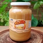 Doce de leite com raspas da Doces Cecília, em pote de vidro com 700 gramas, sobre mesa de madeira.