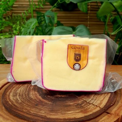 Queijo Gouda Val di Fiemme fracionado e embalado, sobre mesa de madeira.