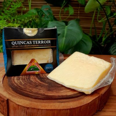 Queijo tipo grana quincas terroir fracionado e embalado, sobre mesa de madeira.