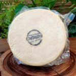 Queijo Pedacin da Serra em peça inteira embalada à vácuo, sobre mesa de madeira.