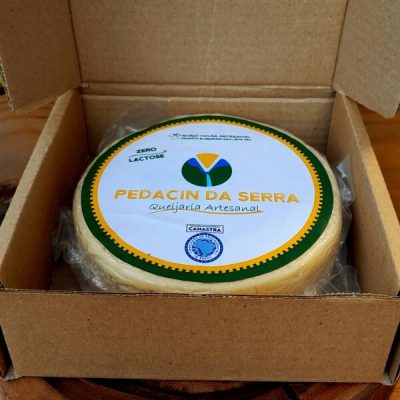 Queijo Canastra Pedacin da Serra em peça inteira embalada à vácuo, sobre mesa de madeira.